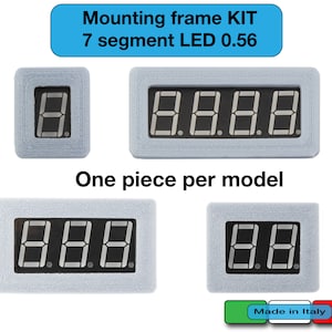 Puede incluir: Cuatro tamaños diferentes de marcos de montaje para pantallas LED de 7 segmentos. Los marcos son de plástico blanco y tienen una superficie texturizada. El texto "Mounting frame KIT 7 segment LED 0.56" está impreso en azul sobre fondo blanco. El texto "One piece per model" está impreso en negro debajo de los marcos. El texto "Made in Italy" está impreso en verde, blanco y rojo sobre fondo blanco.