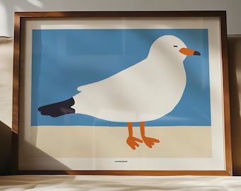 May include: A framed art print featuring a stylized white seagull with a dark tail, orange beak, and orange feet standing on a beige sand surface against a solid blue sky background. The print is enclosed in a simple brown wooden frame.