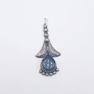 May include: A silver pendant featuring a light blue, teardrop-shaped gemstone. The pendant has a floral design with detailed leaf patterns and small, round accents. The top has small beads and a loop for a chain.