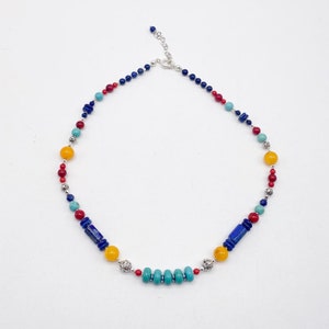 Pu&ograve; includere: Una collana di perline multicolori con perline blu, rosse, gialle e turchesi. La collana ha una chiusura argentata e dettagli argentati.