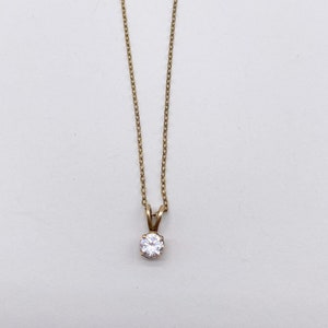 May include: A gold chain necklace with a single, clear, round gemstone pendant.