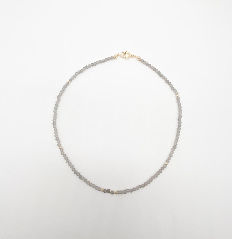 May include: A delicate grey beaded necklace with gold accents and a gold clasp.