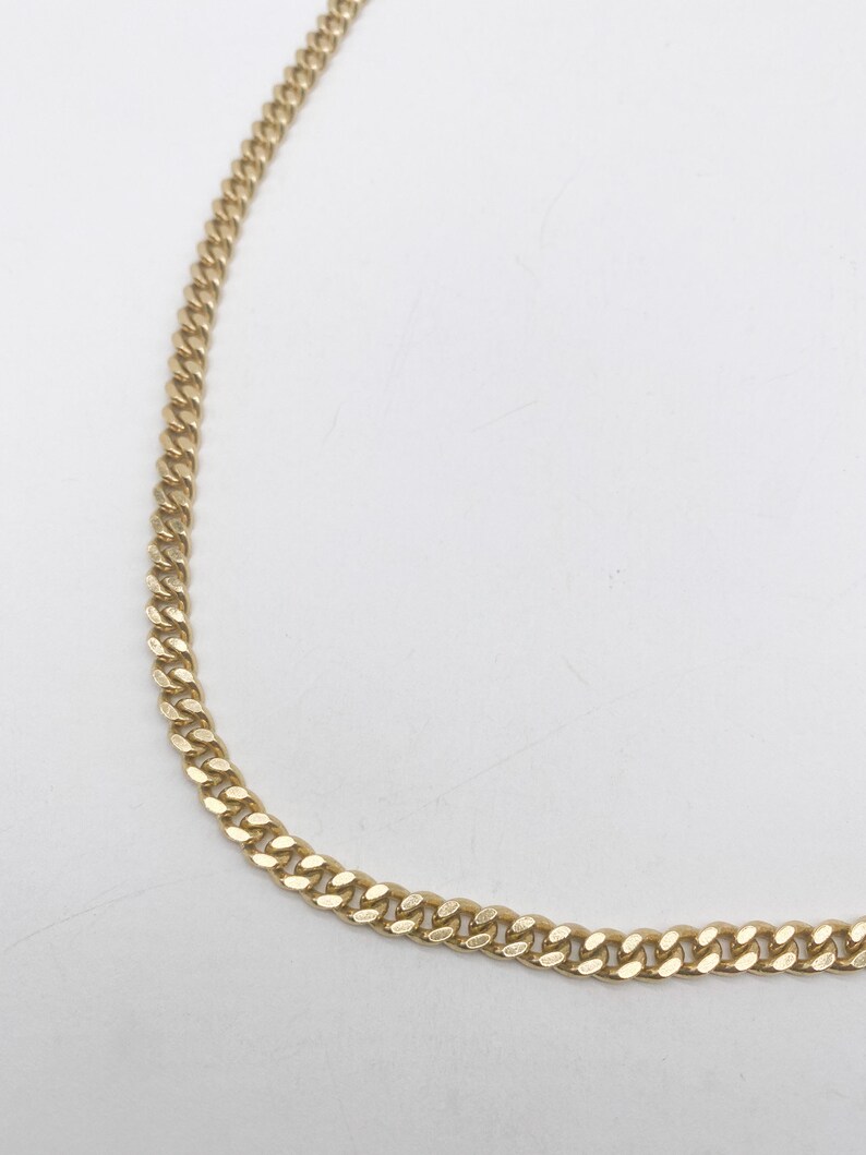 May include: A gold chain necklace with a curb link style.