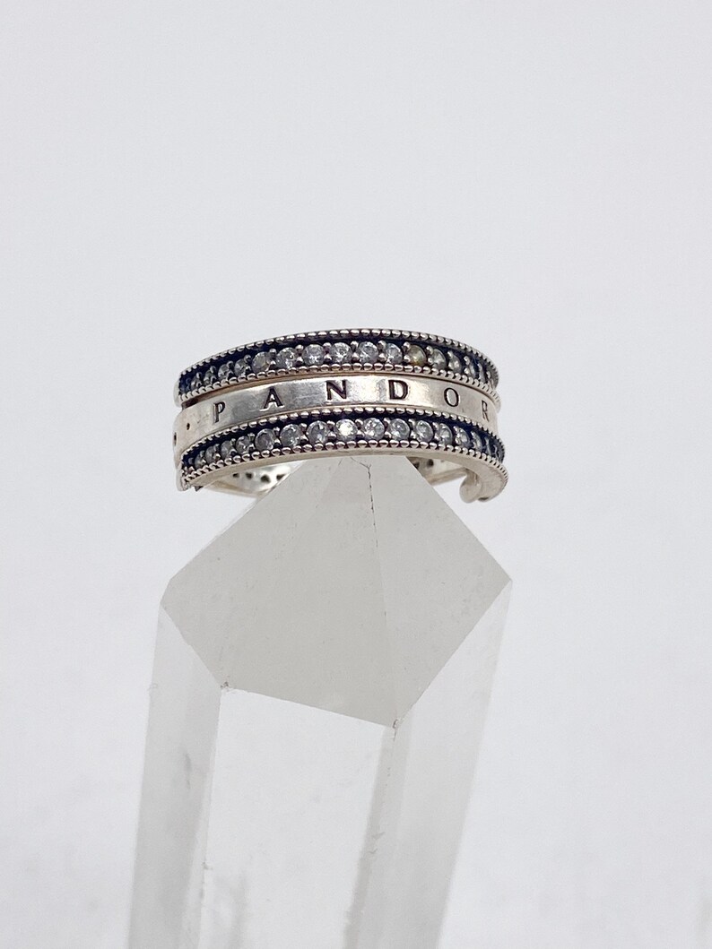 May include: A silver Pandora ring with a double row of clear cubic zirconia stones and the word "Pandora" engraved on the band.