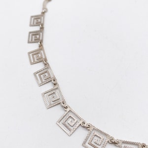 May include: Silver necklace with a chain and multiple square-shaped pendants. Each pendant is made of a silver wire that is twisted into a spiral pattern.