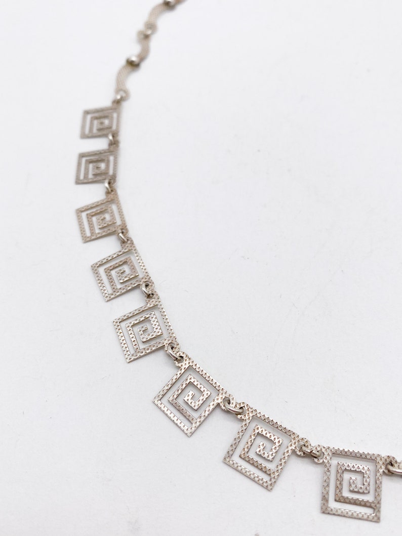 May include: Silver necklace with a chain and multiple square-shaped pendants. Each pendant is made of a silver wire that is twisted into a spiral pattern.