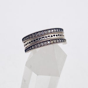May include: A silver ring with three bands, each featuring a row of small clear stones and a delicate heart design.