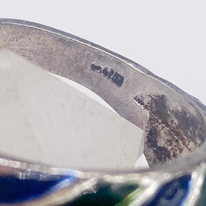 Puede incluir: Primer plano de un anillo de plata con un dise&ntilde;o de esmalte colorido. El anillo presenta un patr&oacute;n de esmalte azul, verde y blanco. El anillo est&aacute; hecho de plata y tiene un acabado liso y pulido.