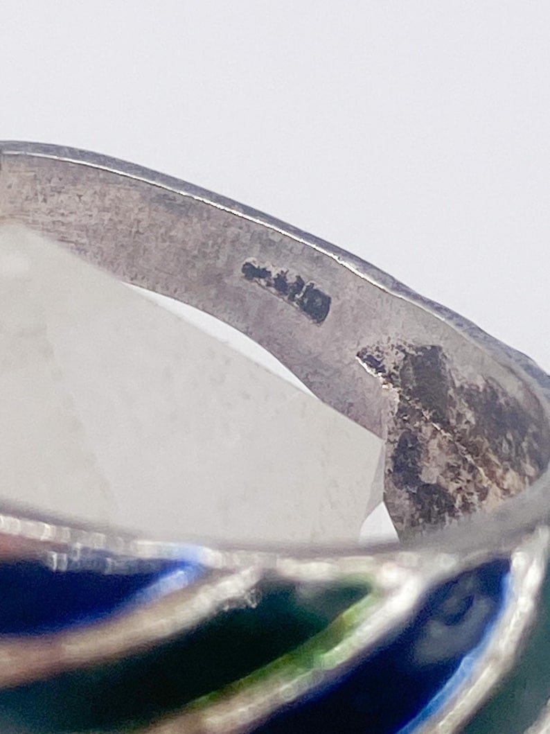 Puede incluir: Primer plano de un anillo de plata con un dise&ntilde;o de esmalte colorido. El anillo presenta un patr&oacute;n de esmalte azul, verde y blanco. El anillo est&aacute; hecho de plata y tiene un acabado liso y pulido.