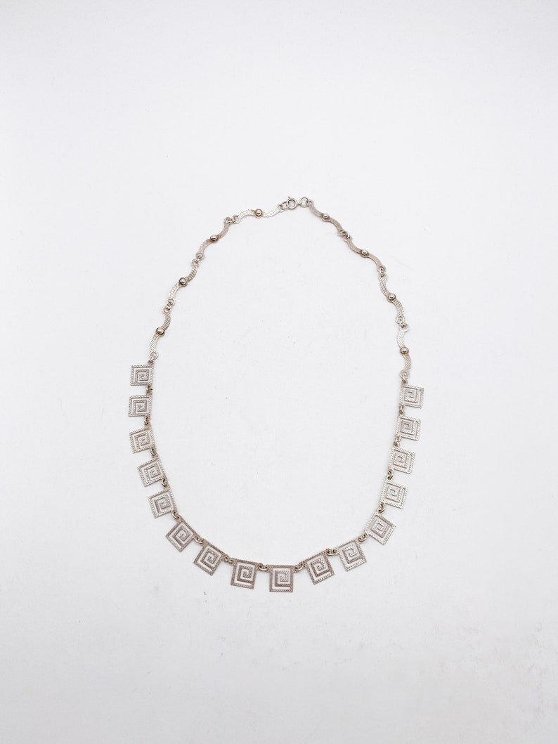 May include: A silver necklace with a delicate chain and square pendants featuring a geometric pattern.