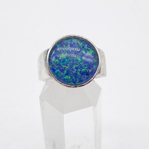 May include: A silver ring featuring a blue opal gemstone. The opal displays green and purple flashes of colour.
