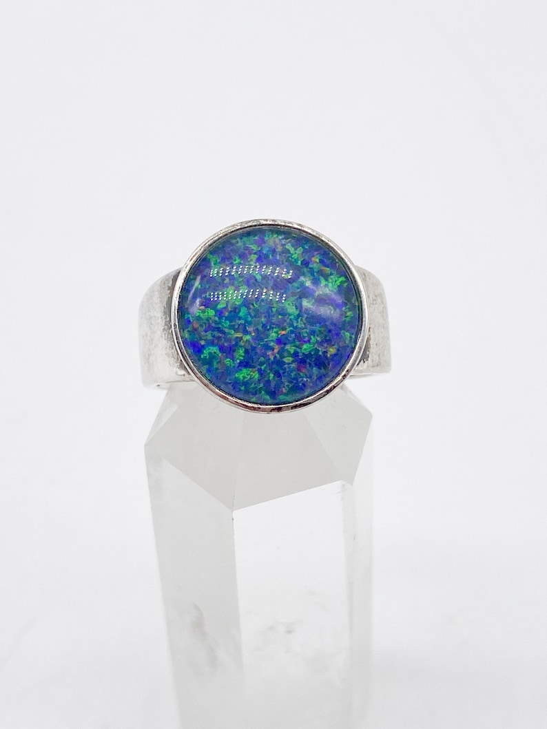 May include: A silver ring featuring a blue opal gemstone. The opal displays green and purple flashes of colour.