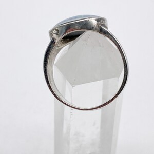May include: A silver ring with a blue opal gemstone set in a bezel setting. The ring is displayed on a clear crystal stand.