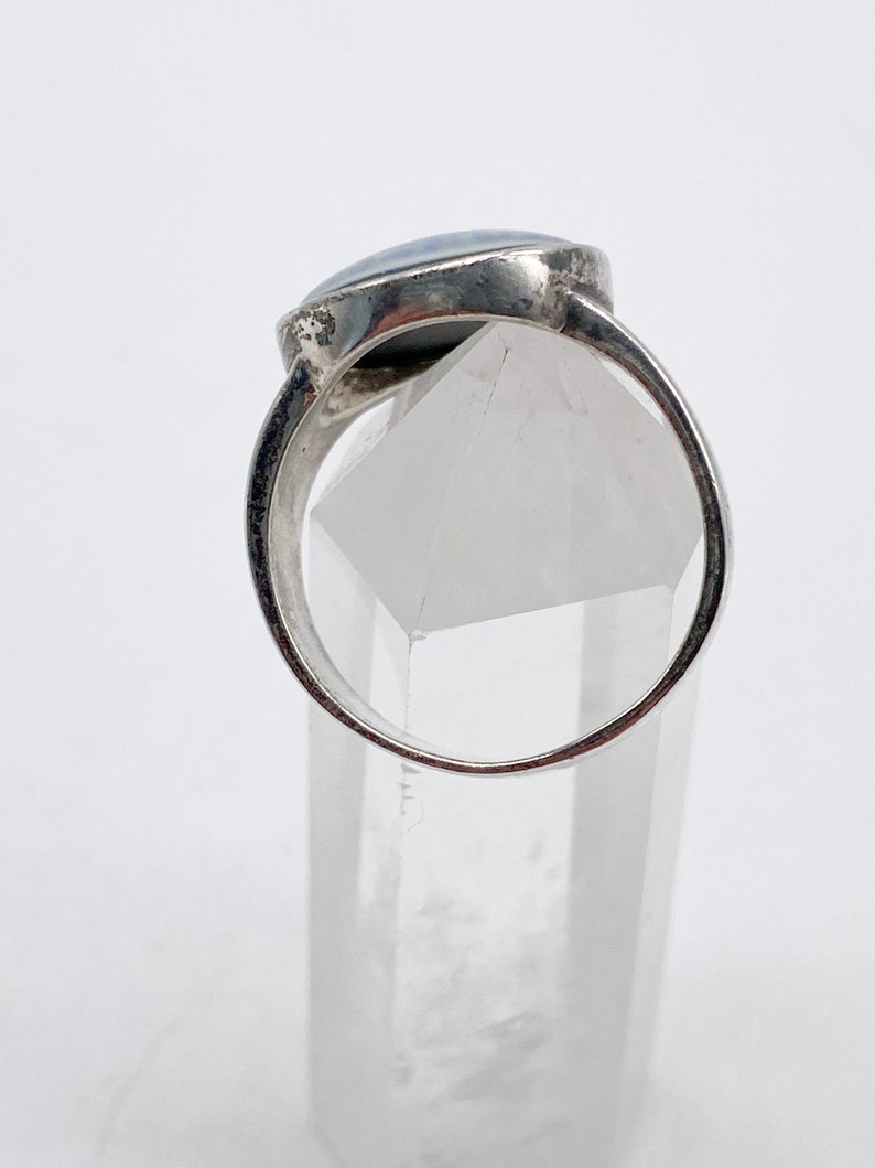 May include: A silver ring with a blue opal gemstone set in a bezel setting. The ring is displayed on a clear crystal stand.