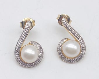 May include: A pair of gold-toned drop earrings with a white pearl center and a swirl design encrusted with small, clear stones. The earrings have a post-back closure.
