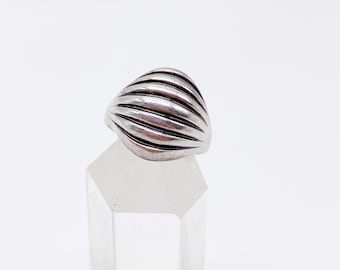 May include: A silver ring with a ribbed design. The ring has a rounded, dome-like shape with horizontal ridges across the surface. The ring is displayed on a clear, faceted crystal. The background is plain white.