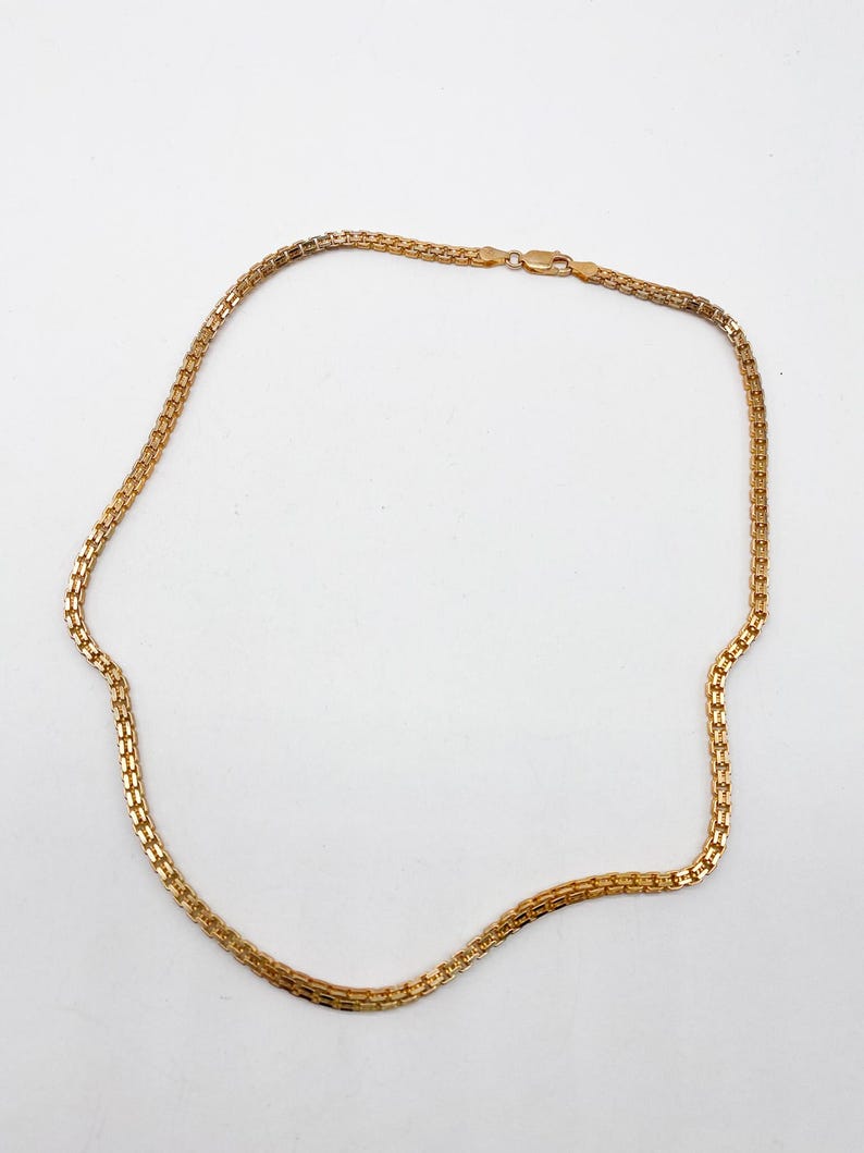 Pu&ograve; includere: Una collana a catena d'oro con un design a catena a scatola.