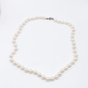 May include: A classic pearl necklace with a silver clasp. The necklace features a strand of round, creamy white pearls, evenly spaced along the strand. The pearls are strung together, forming a complete circle. The clasp is a simple, secure design.
