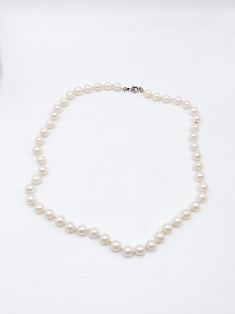 May include: A classic pearl necklace with a silver clasp. The necklace features a strand of round, creamy white pearls, evenly spaced along the strand. The pearls are strung together, forming a complete circle. The clasp is a simple, secure design.