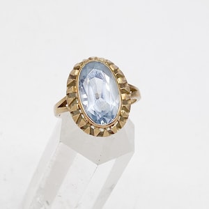 May include: A gold ring with a light blue oval-shaped gemstone set in a decorative gold frame.