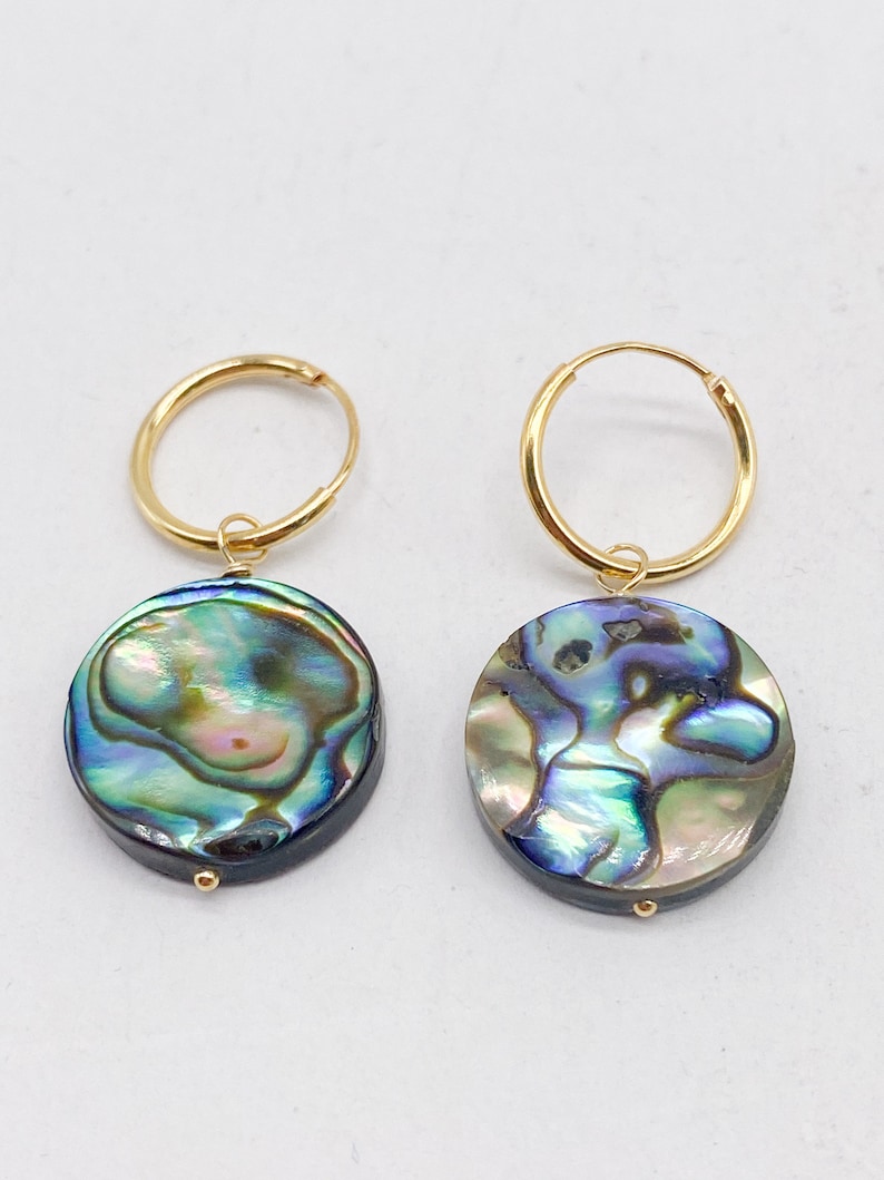 May include: A pair of gold hoop earrings with a round iridescent abalone shell pendant on each earring.