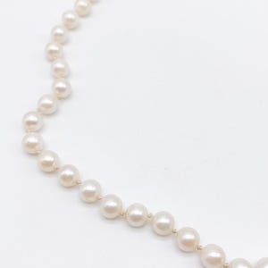 May include: A strand of off-white pearls, arranged in a necklace. The pearls are round and have a subtle luster. The necklace is set against a white background, highlighting the delicate design and the color of the pearls.