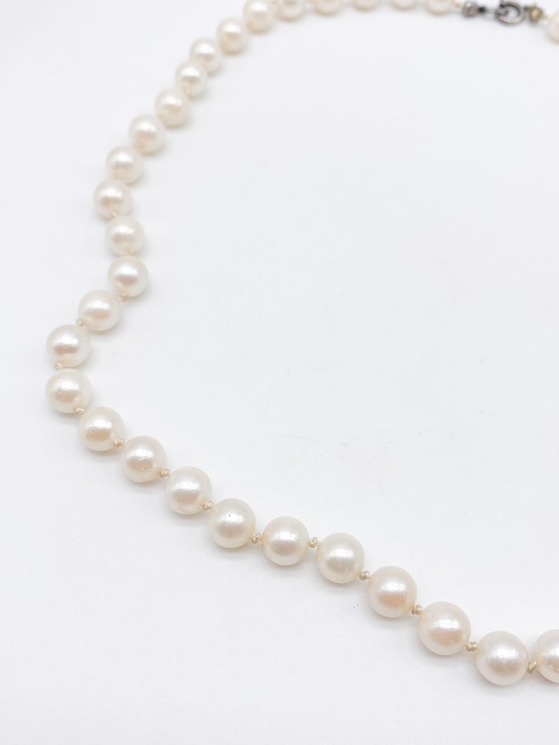 May include: A strand of off-white pearls, arranged in a necklace. The pearls are round and have a subtle luster. The necklace is set against a white background, highlighting the delicate design and the color of the pearls.