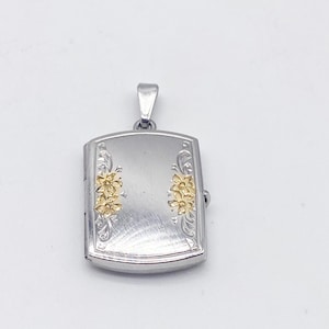 May include: Silver-tone rectangular locket pendant with gold-colored floral accents. The locket has a hinged design and a small loop for a chain. The floral details are on the front of the locket.