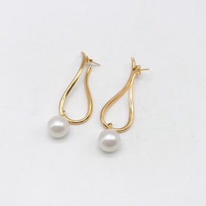 May include: A pair of gold-toned earrings featuring a smooth, curved, open teardrop-shaped metal frame. Each earring is accented with a single, round, white pearl suspended from the bottom of the metal loop, complete with a standard post backing.