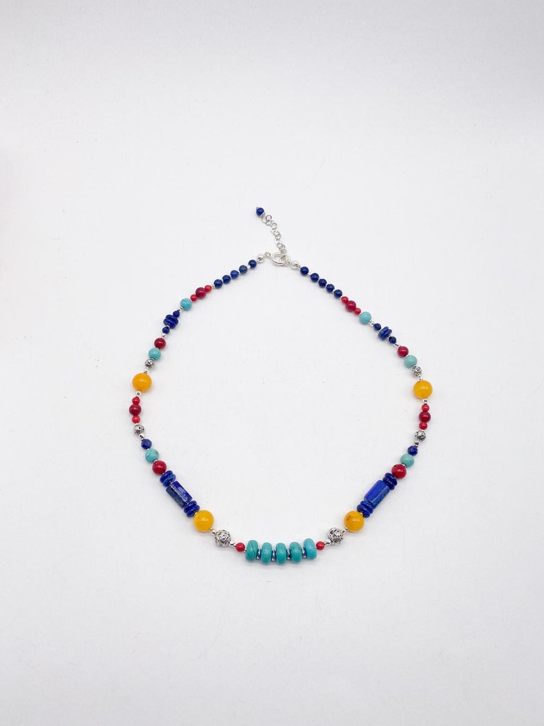 Pu&ograve; includere: Una collana di perline multicolori con perline blu, rosse, gialle e turchesi. La collana ha una chiusura argentata e dettagli argentati.