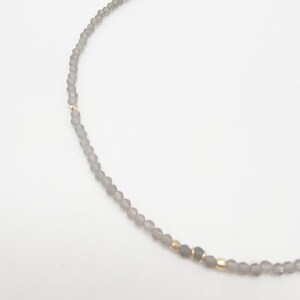 May include: A delicate gray beaded necklace with gold accents. The necklace is made of small, round beads and has a simple, elegant design.
