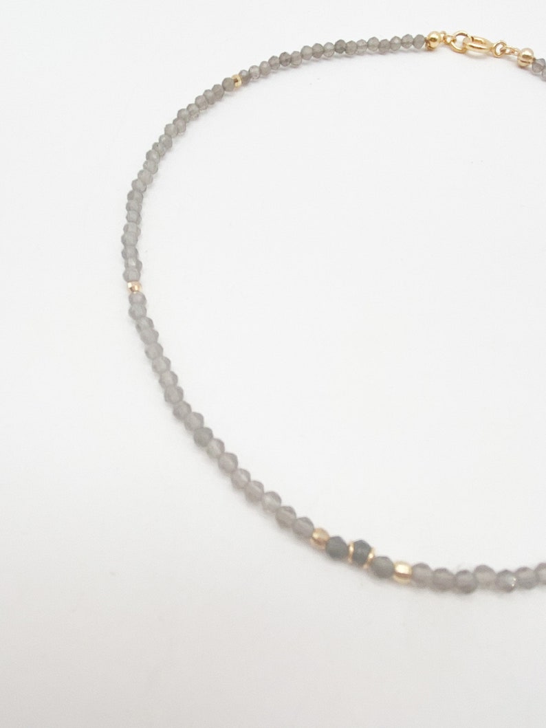 May include: A delicate gray beaded necklace with gold accents. The necklace is made of small, round beads and has a simple, elegant design.