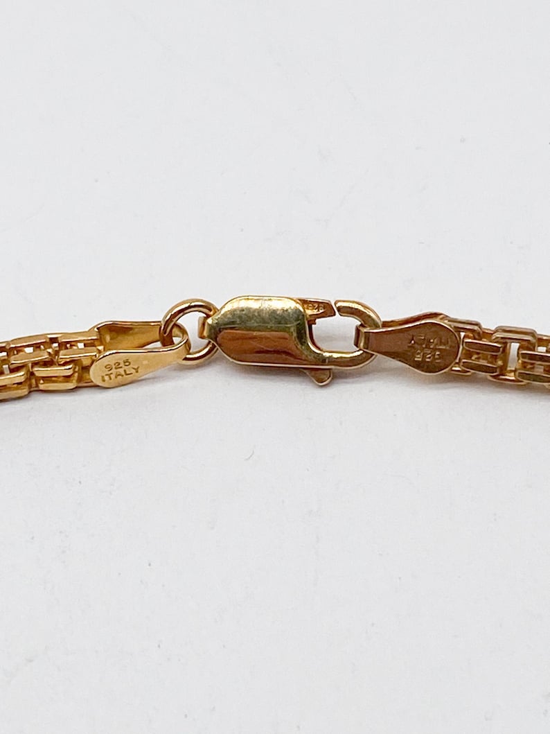 Pu&ograve; includere: Primo piano di una chiusura di collana a catena d'oro con l'iscrizione "925 ITALY" su un lato e "925" sull'altro.