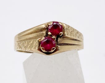 May include: A gold ring with two bright red gemstones. The ring has a textured band and a traditional design. The gemstones are set in a raised setting, enhancing the ring's elegance. This is a classic piece of jewellery.