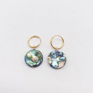 May include: A pair of gold hoop earrings with a round abalone shell pendant. The shell has a blue, green, and iridescent color.
