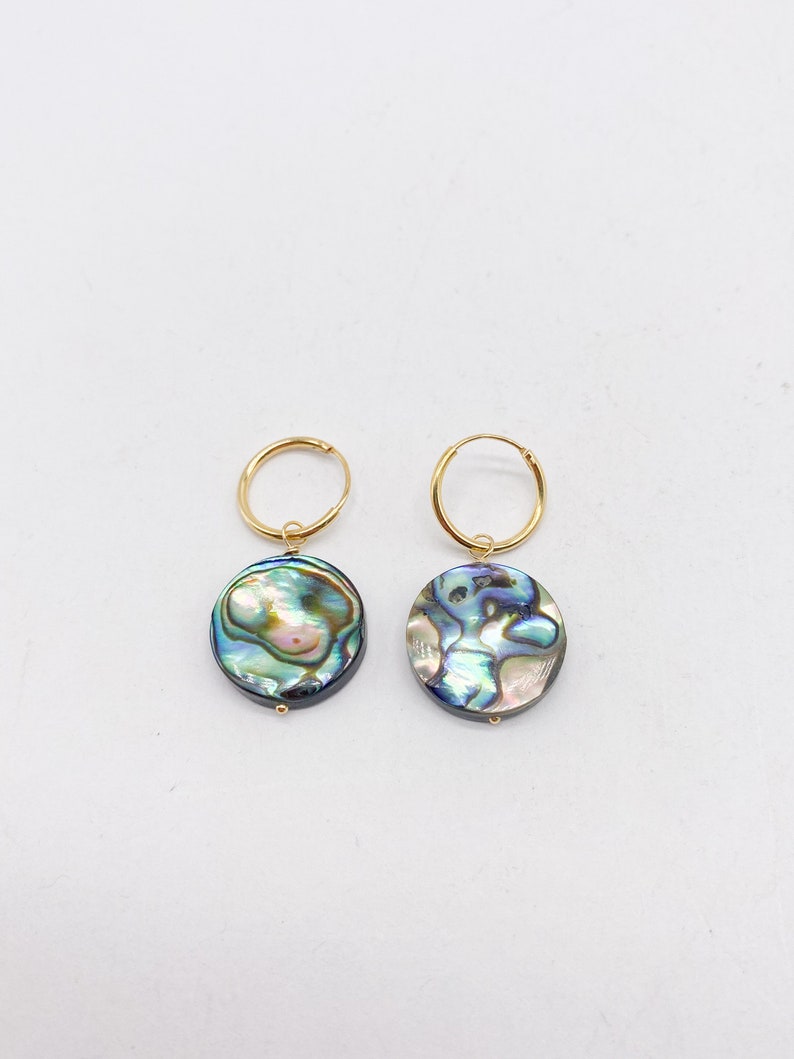 May include: A pair of gold hoop earrings with a round abalone shell pendant. The shell has a blue, green, and iridescent color.