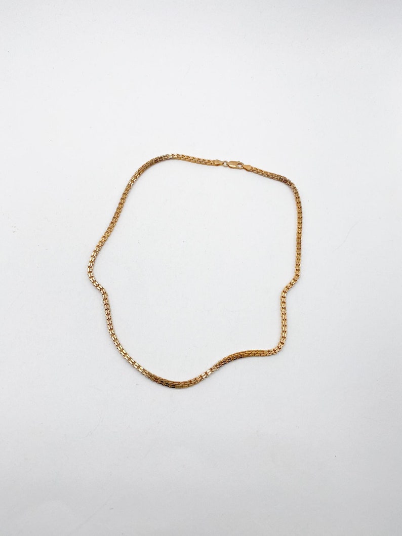 Pu&ograve; includere: Una collana a catena d'oro con un design a catena a scatola. La catena &egrave; posata piatta su una superficie bianca.