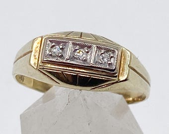 Puede incluir: Un anillo de oro con tres pequeños diamantes engastados en un rectángulo. El anillo tiene un diseño texturizado en la cara y una banda de oro pulido. Los diamantes están engastados en un metal blanco, contrastando con el oro.