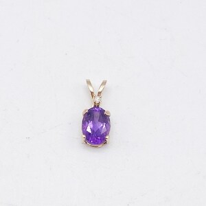 May include: A gold pendant featuring an oval, deep purple gemstone. The pendant has a small, round, clear stone set above the purple stone. The pendant is suspended from a gold bail.