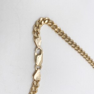 May include: A gold chain necklace with a curb link style. The chain is shown laying flat on a white surface.