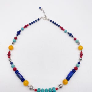 Pu&ograve; includere: Una collana di perline colorate con perline blu, rosse, gialle e turchesi. La collana ha una chiusura argentata.
