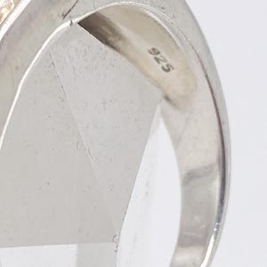 May include: Close-up of a silver ring with a 925 stamp. The ring has a polished finish and a simple design. The ring is likely made of sterling silver.