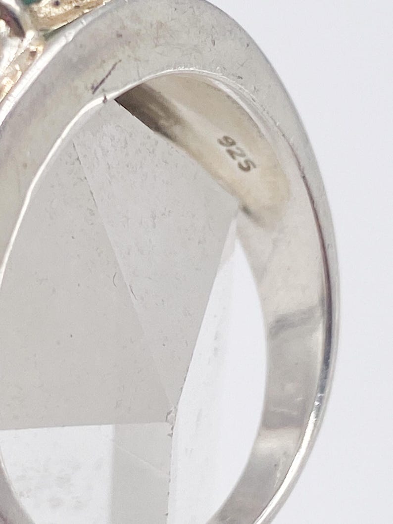 May include: Close-up of a silver ring with a 925 stamp. The ring has a polished finish and a simple design. The ring is likely made of sterling silver.