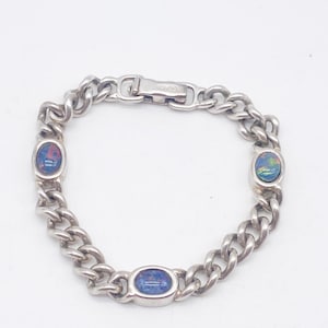 Puede incluir: Pulsera plateada con diseño de cadena de eslabones. La pulsera tiene tres piedras de ópalo ovaladas con colores iridiscentes. El cierre es un cierre de gancho y ojo simple. Una joya clásica.