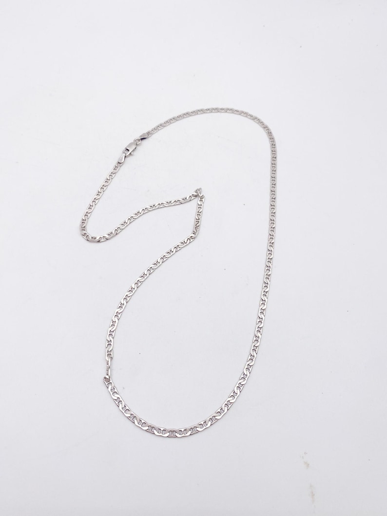 May include: A silver-colored chain necklace with a delicate, linked design. The necklace is displayed against a plain white background, highlighting its simple elegance. The chain is likely made of a precious metal.