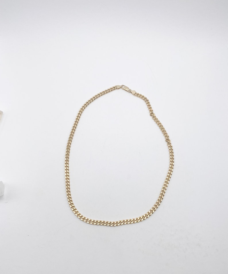 May include: A gold chain necklace with a curb link style. The chain is about 18 inches long.