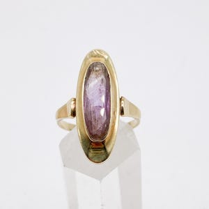 May include: A gold ring with a purple oval gemstone set in a bezel setting.