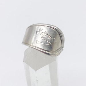 Pode incluir: Um anel de prata com um design estilizado de dois pássaros que se olham. O anel é feito de uma colher reutilizada.