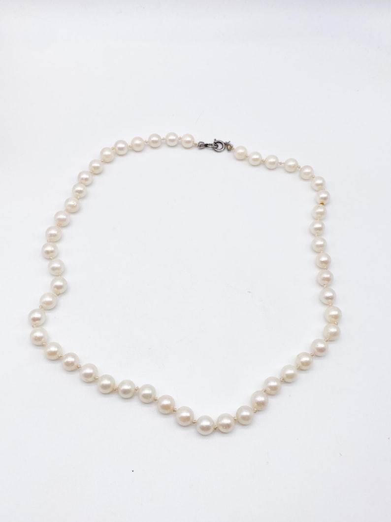 May include: A delicate necklace composed of numerous round, off-white pearls. The pearls are strung together, forming a continuous strand that fastens with a small, silver-toned clasp. The necklace is displayed against a plain white background.