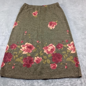 May include: A midi-length skirt in a heathered olive green knit fabric featuring a floral pattern of pink and deep red roses with green leaves. The skirt has an elasticized waistband and a straight silhouette with a dense rose print at the hem.